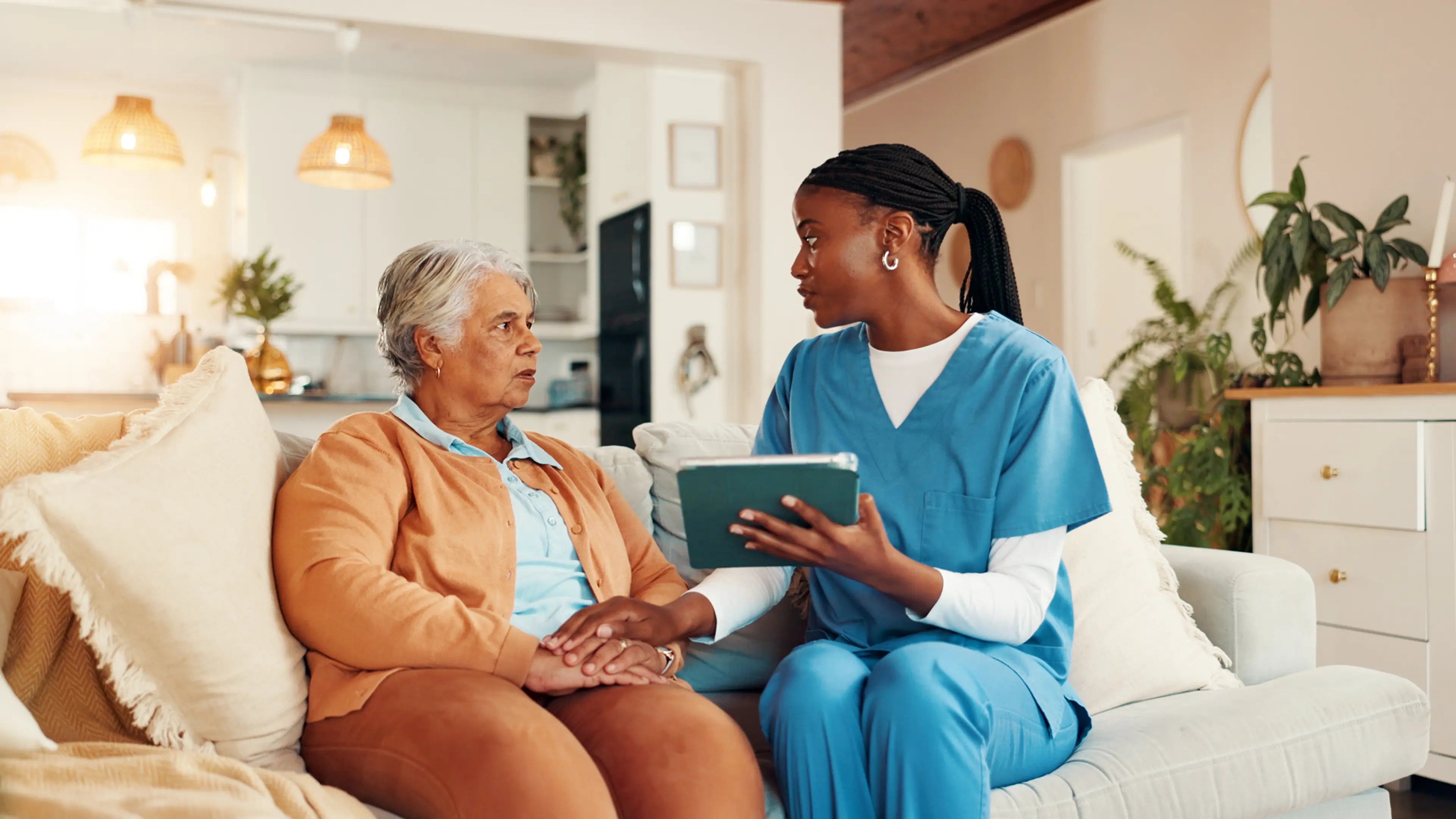 Nurse, senior woman and holding hands with tablet on sofa for report with medical results, feedback or bad news. Caregiver, elderly person and stress with touchscreen, app and consultation in home