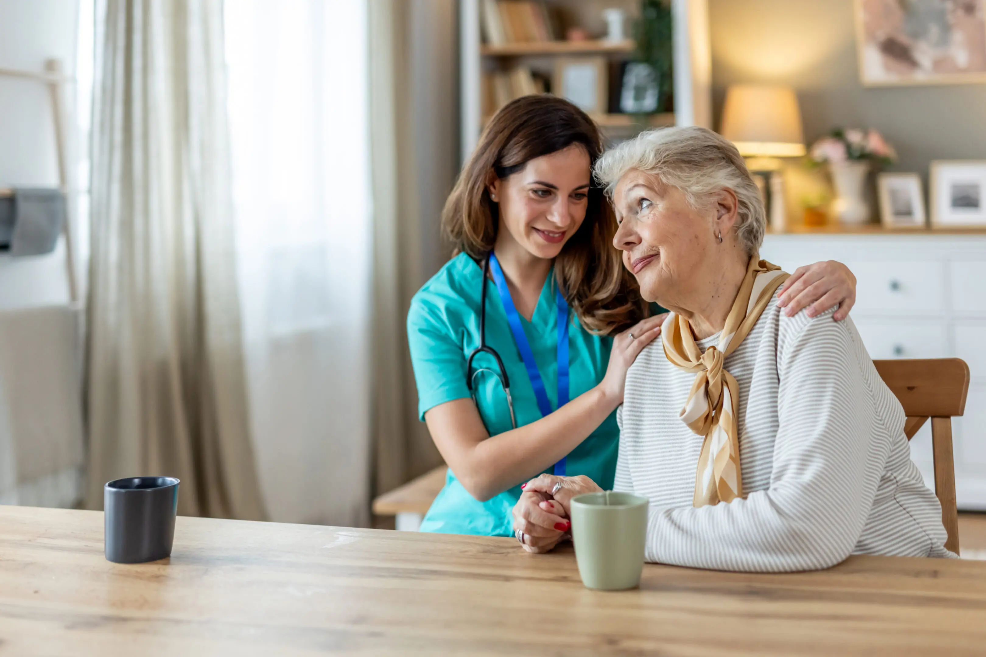 A compassionate caregiver shares a moment of support and kindness with an elderly woman in a cozy home setting, symbolizing care, trust, and companionship during healthcare assistance.